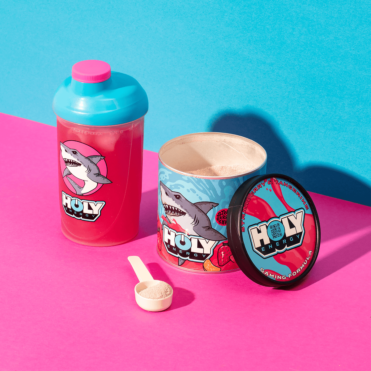 Bunte Pappdose, gefüllt mit Pulver, daneben ein Shaker und ein Messlöffel, auf pink-blauem Hintergrund.
