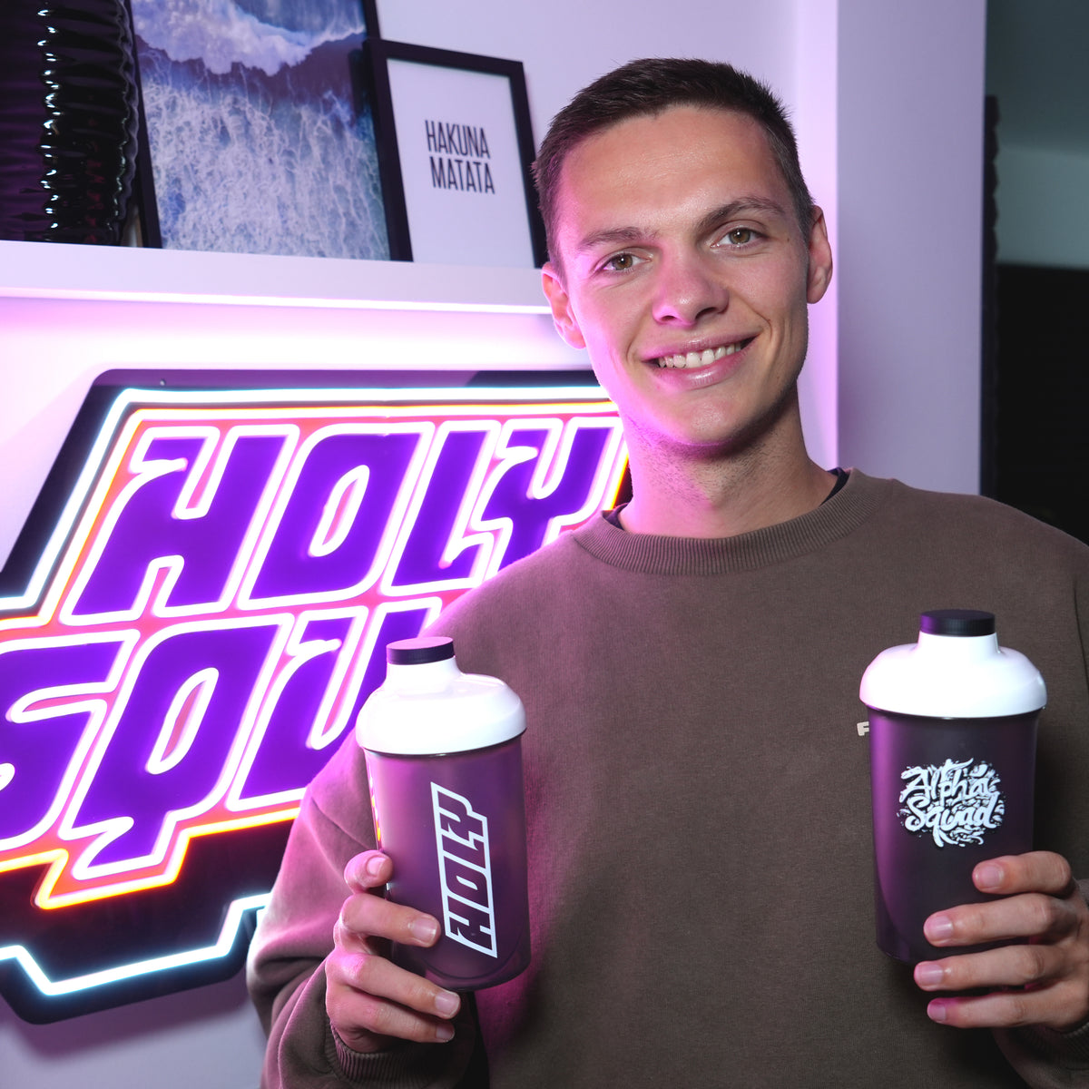 Ein Mann hält zwei Shaker in den Händen vor einem leuchtenden "Holy Squad"-Schild.