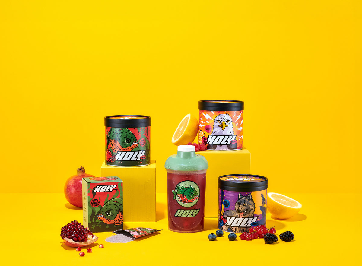 Verschiedene bunte Pappdosen und ein Shaker auf gelbem Hintergrund, umgeben von Früchten und Sachets.