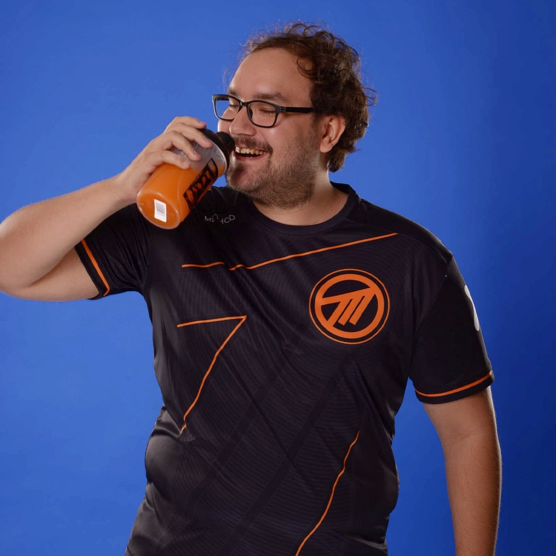 Mann mit Brille trinkt aus einem orangefarbenen Shaker vor blauem Hintergrund.
